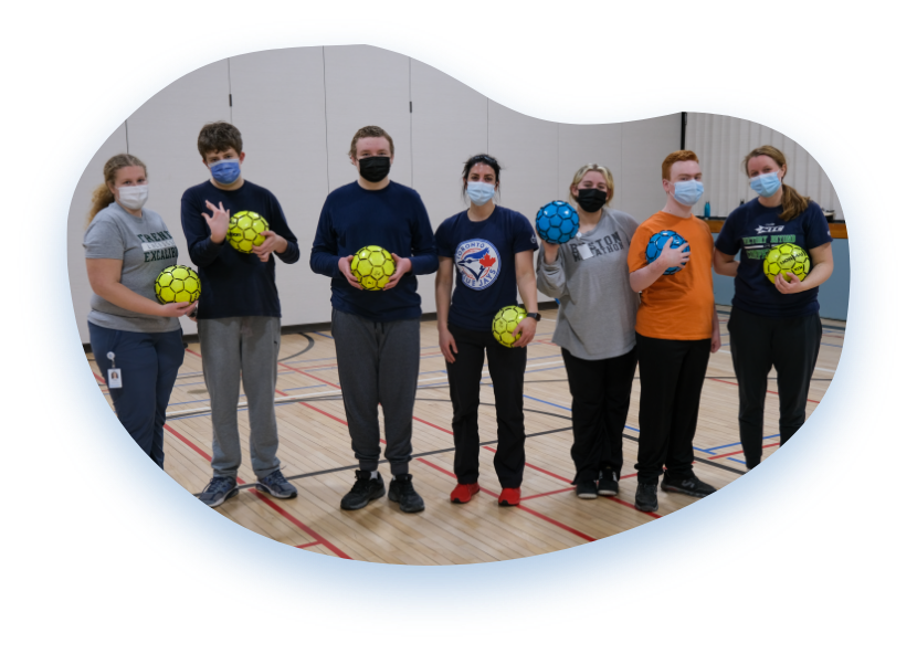 A group of youth stand, wearing masks, and holding sports balls ready to engage in a fun game together.